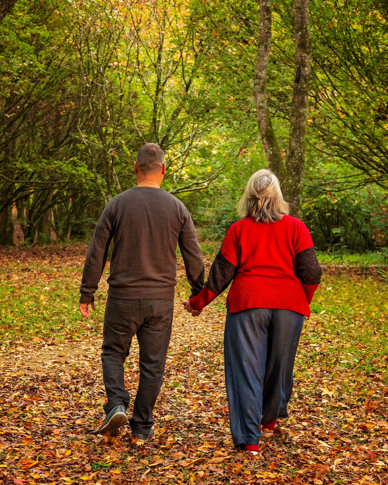 An older couple walking hand in hand along a path covered in autumn leaves