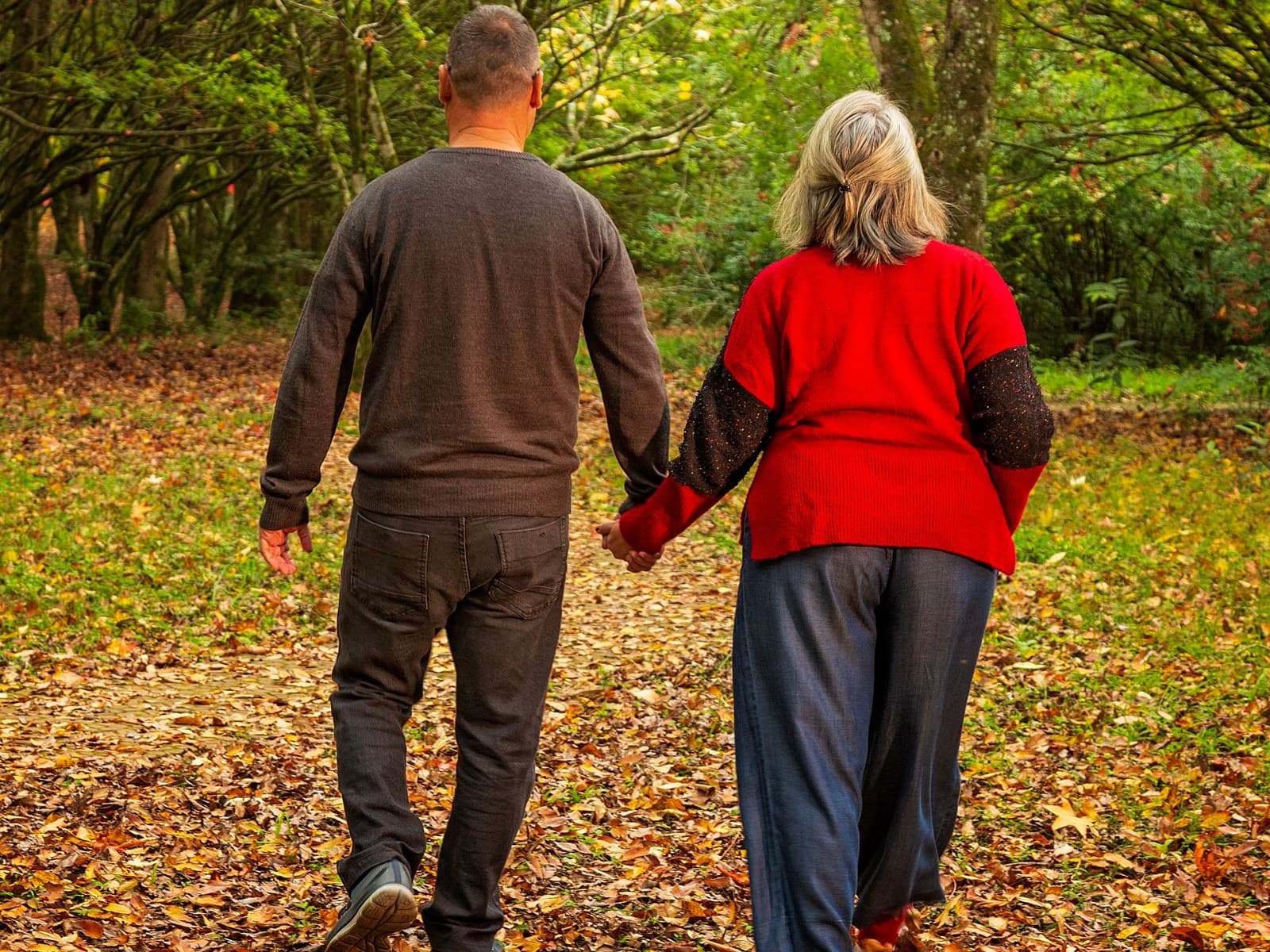 An older couple walking hand in hand along a path covered in autumn leaves