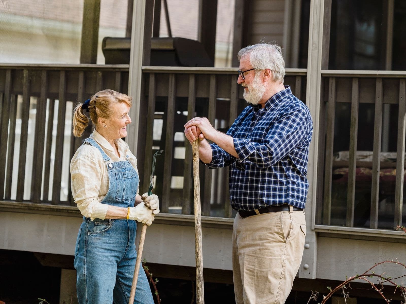 An older couple standing in front of their porch, talking, garden tools in hand