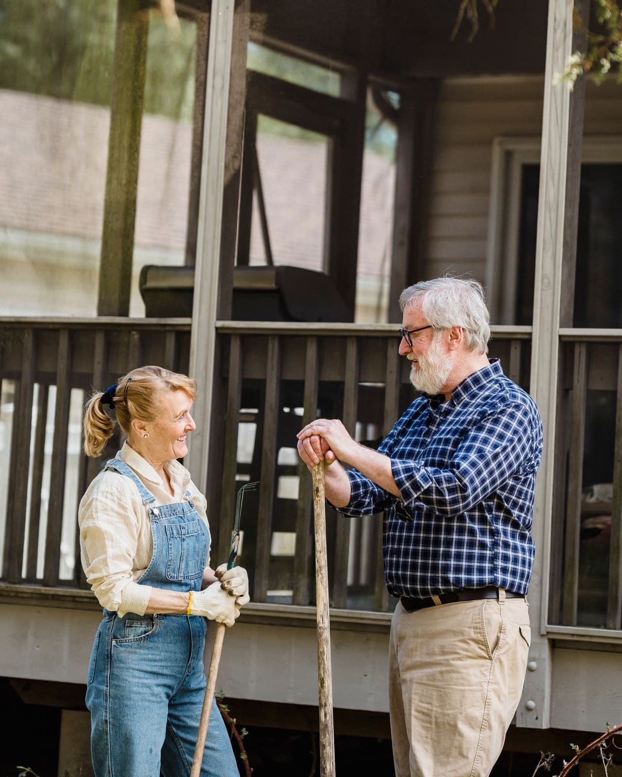 An older couple standing in front of their porch, talking, garden tools in hand